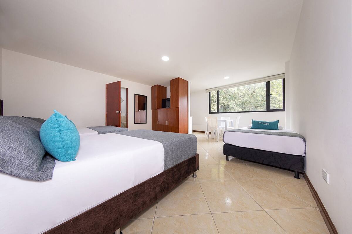 Une chambre moderne avec un grand lit, un lit plus petit, une armoire et une fenêtre donnant sur des arbres.
