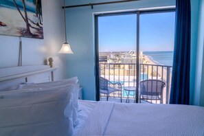 Habitación de hotel con cama, un cuadro y balcón con vistas a la playa y al paisaje urbano.