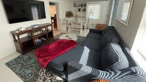 A living room with a large flat-screen TV, a sofa, a coffee table, and a patterned rug. -     Private Tropical Oasis in Coastal Paradise
W fenced yard. (Clearwater)