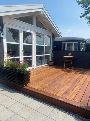 Eine Holzterrasse mit einer Schiebetür, einem kleinen Tisch und einem Blumenkasten.