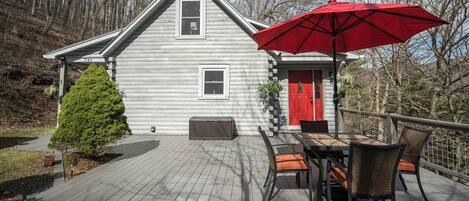 Una terraza de madera con una mesa de comedor y sillas, un paraguas rojo y una casa con puerta roja.
