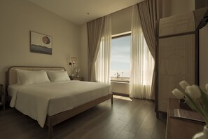 Een slaapkamer met een groot bed, uitzicht op palmbomen en een raam met dunne gordijnen.