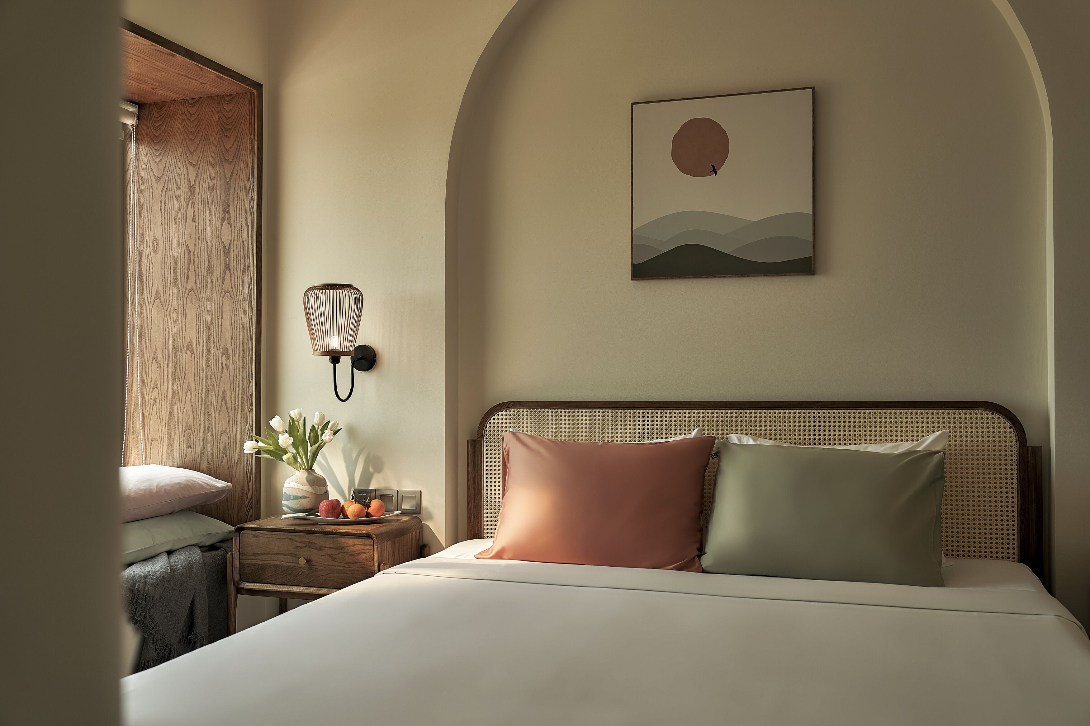Une chambre à coucher avec un lit, une table de chevet, une lampe et une œuvre d’art accrochée au mur.