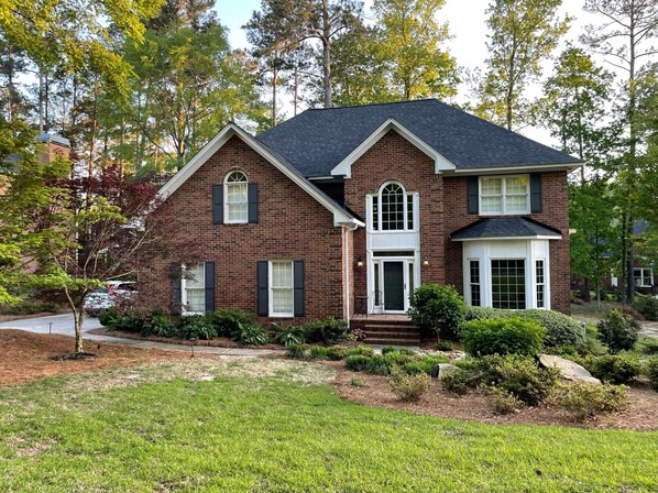 A two-story brick house with a gabled roof, a front porch, and a well-maintained front yard with shrubs and a lawn. - Martinez Masters Home (Martinez)