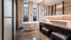 A modern bathroom with a freestanding bathtub, a large vanity with a mirror, and a city view through large windows.