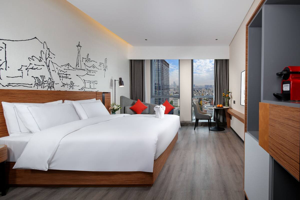 Une chambre d’hôtel moderne dotée d’un grand lit, offrant une vue sur la ville, comprenant un coin repas et une kitchenette.