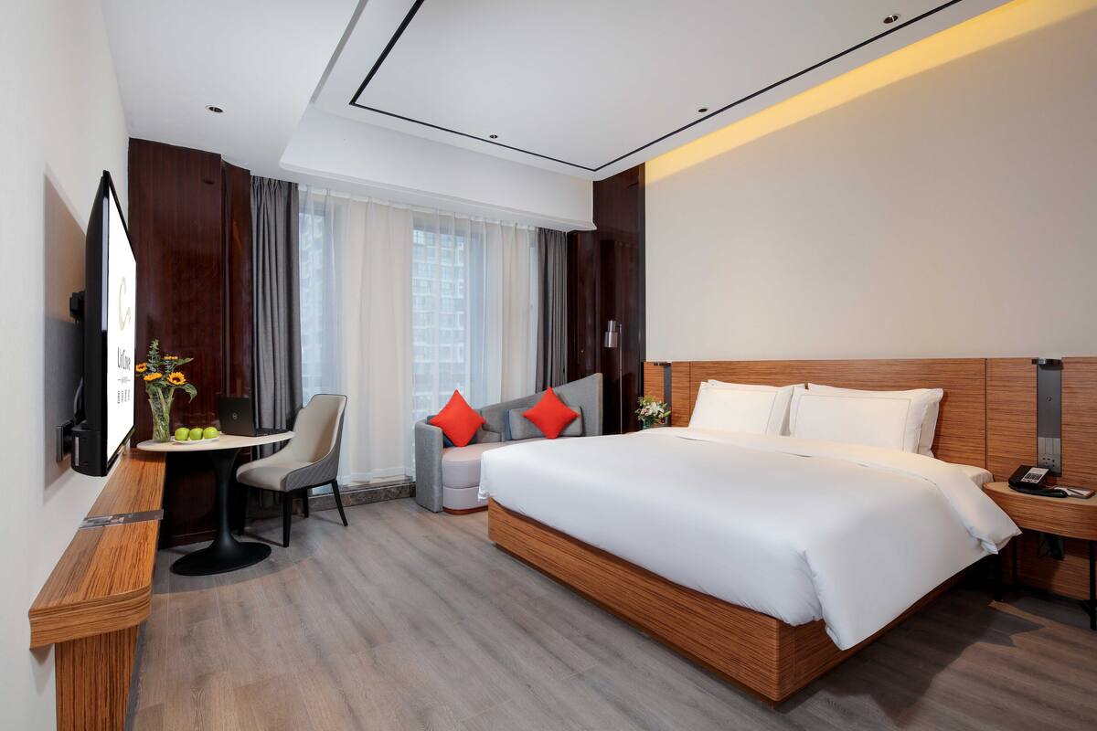 Une chambre d’hôtel moderne avec un grand lit, un bureau avec une chaise, une petite table avec un vase et un téléviseur fixé au mur.