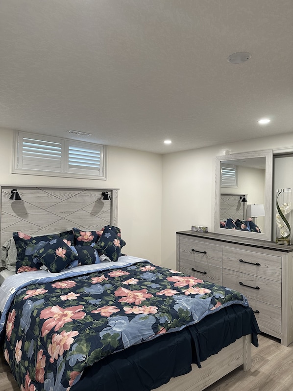 Un dormitorio con cama, cómoda, espejo y ventana con persianas.