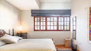A bedroom with a bed, a window with a view, a bedside lamp, and a small round table. - Hot Springs pool in historic Baños del Inca, 10 min. from Cajamarca, sleeps 6 (Cajamarca)