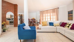 A living room with a blue armchair, a white sofa, and a dining area with a table and chairs. - Hot Springs pool in historic Baños del Inca, 10 min. from Cajamarca, sleeps 6 (Cajamarca)