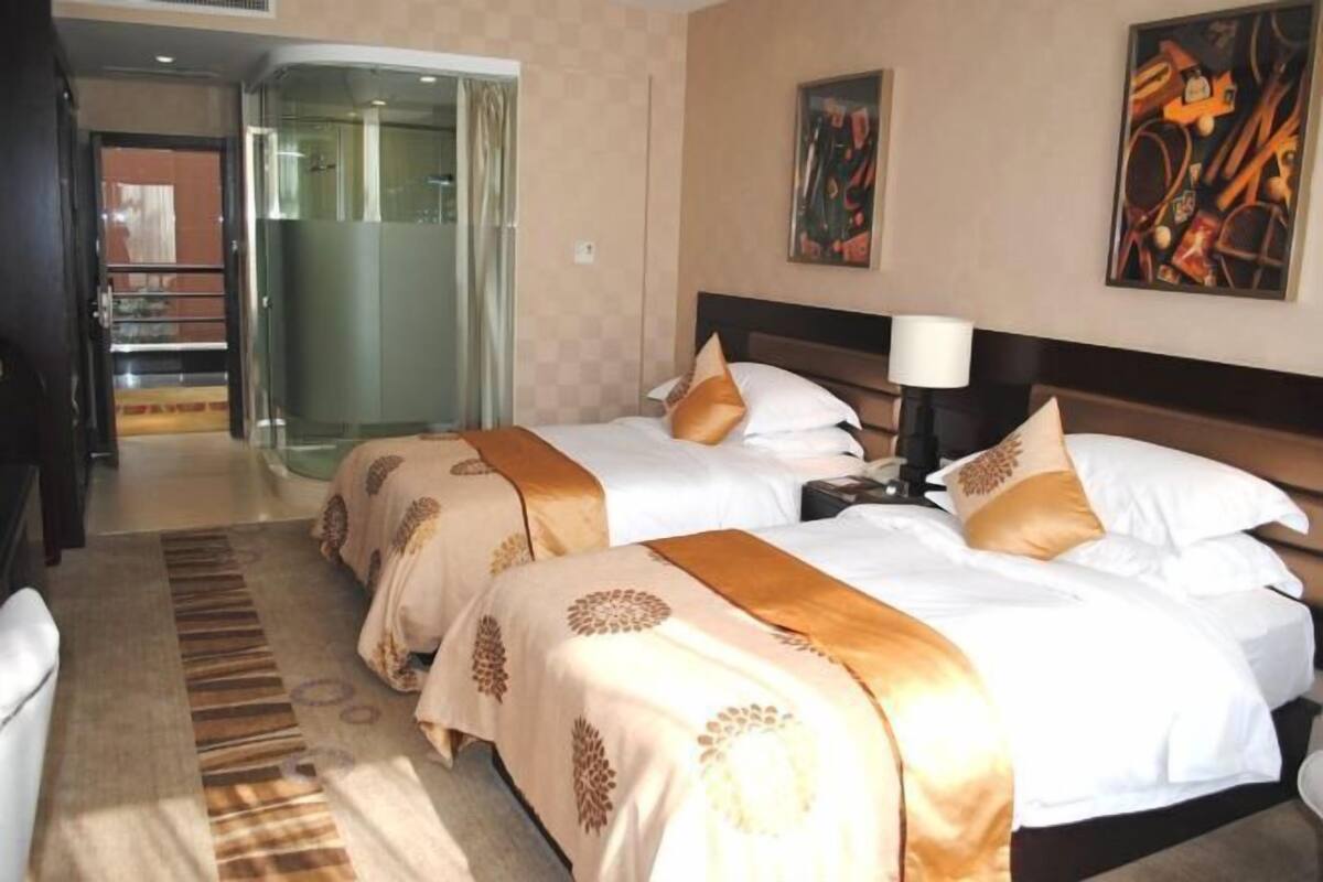 Una habitación de hotel con dos camas, una puerta de cristal que da a un balcón y obras de arte en las paredes.