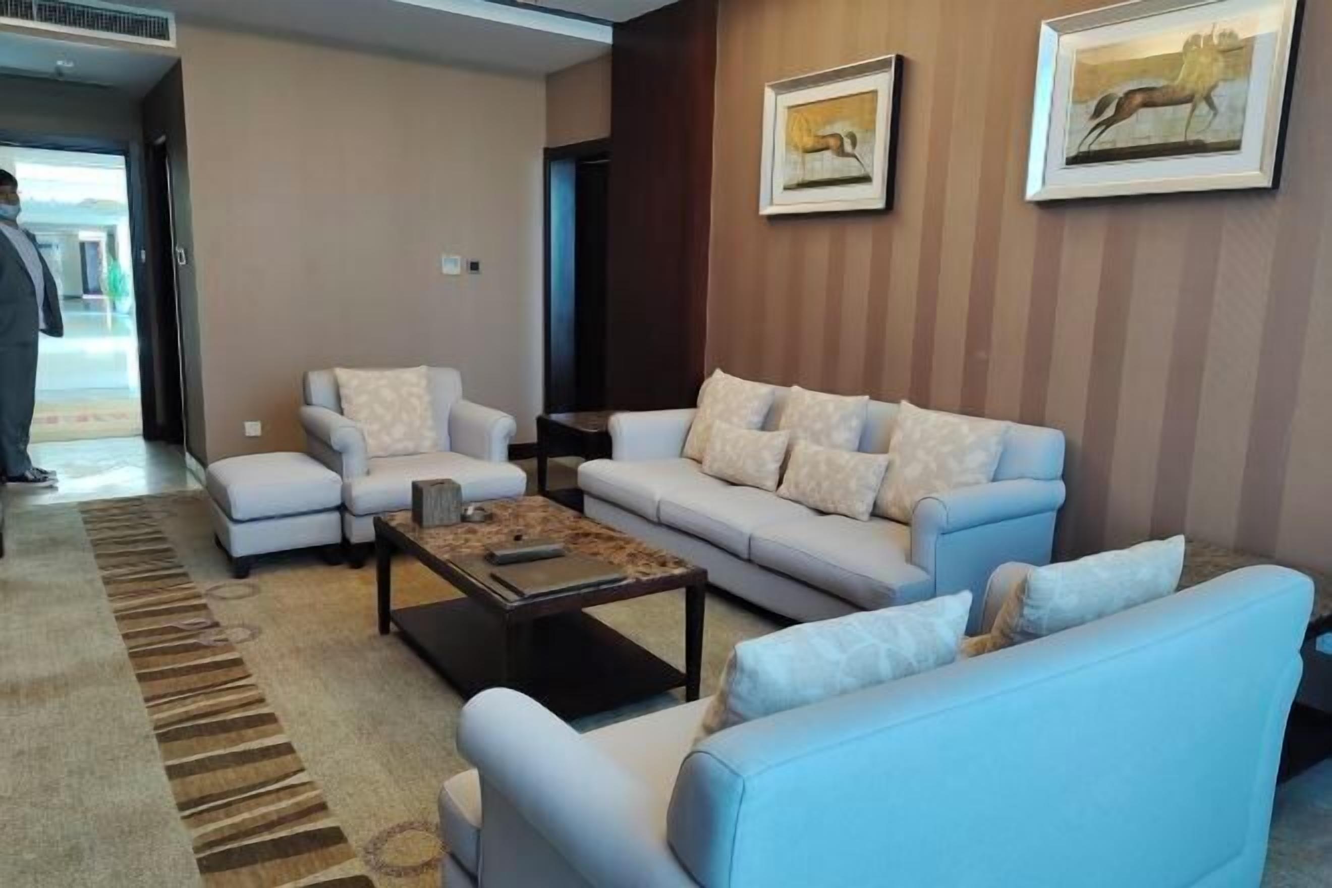 A modern living room with a light blue sofa, a matching armchair, and a coffee table. There are two framed pictures on the wall.