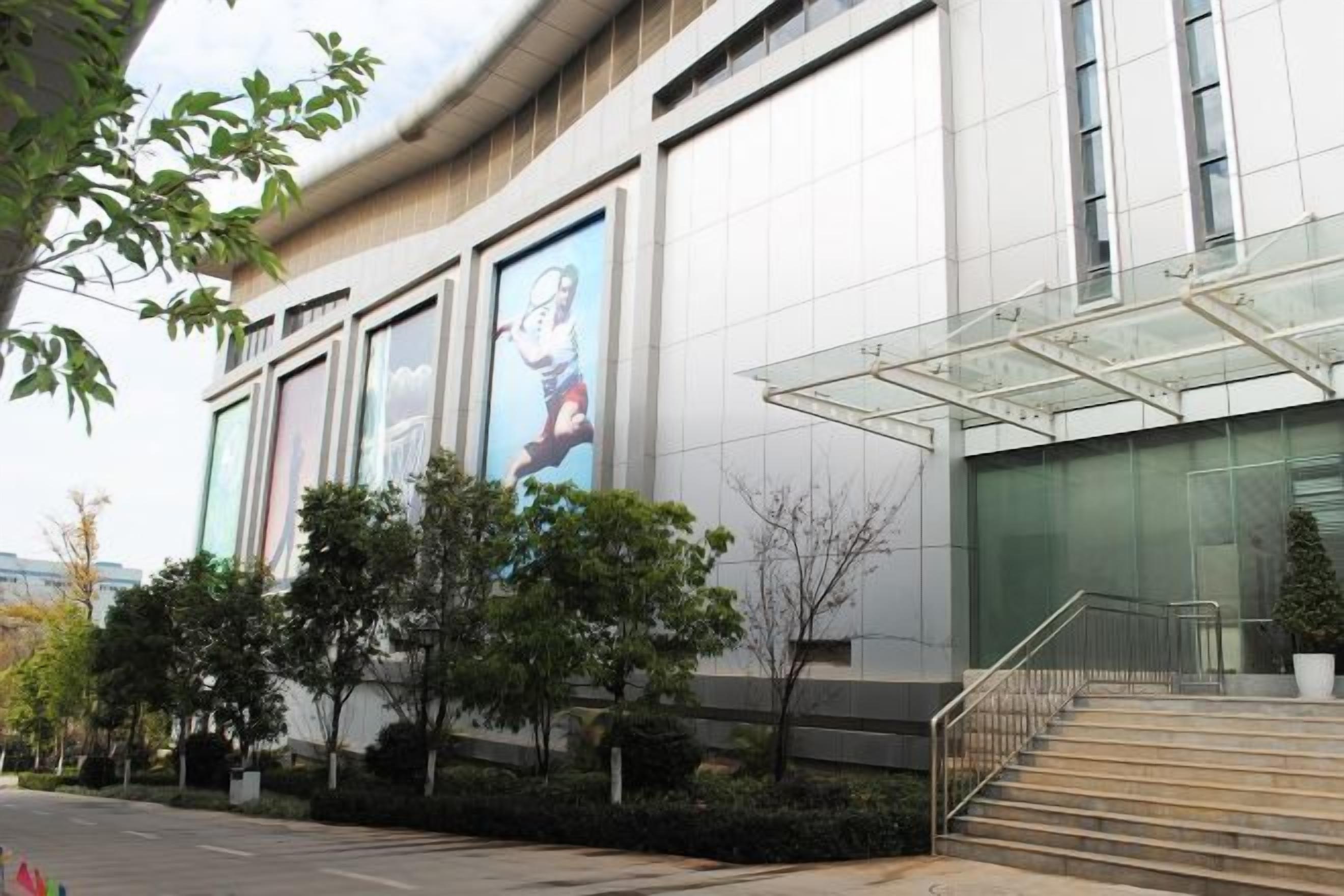 A modern building with a glass entrance, steps leading up to it, and a large digital billboard on the side.