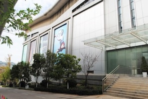 Un bâtiment moderne avec une entrée en verre, des marches menant à l’entrée et un grand panneau publicitaire numérique sur le côté.