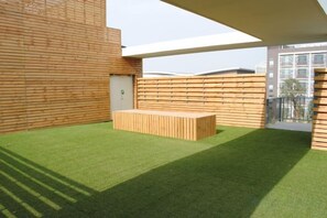 Un espacio exterior con césped artificial, un banco de madera y una estructura de edificio moderna al fondo.