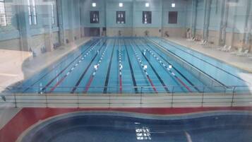 Una amplia piscina interior con múltiples carriles, zona para espectadores y área de descanso cubierta.