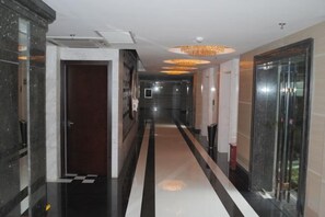 Een hotelgang met een zwart-wit geruit vloerkleed, een kroonluchter en een glazen lift.