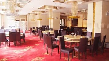 A hotel dining area with round tables, chairs, and chandeliers.