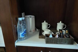 Una kitchenette equipada con cafetera, botellas de agua, bolsitas de té y una bandeja con tazas y tetera.