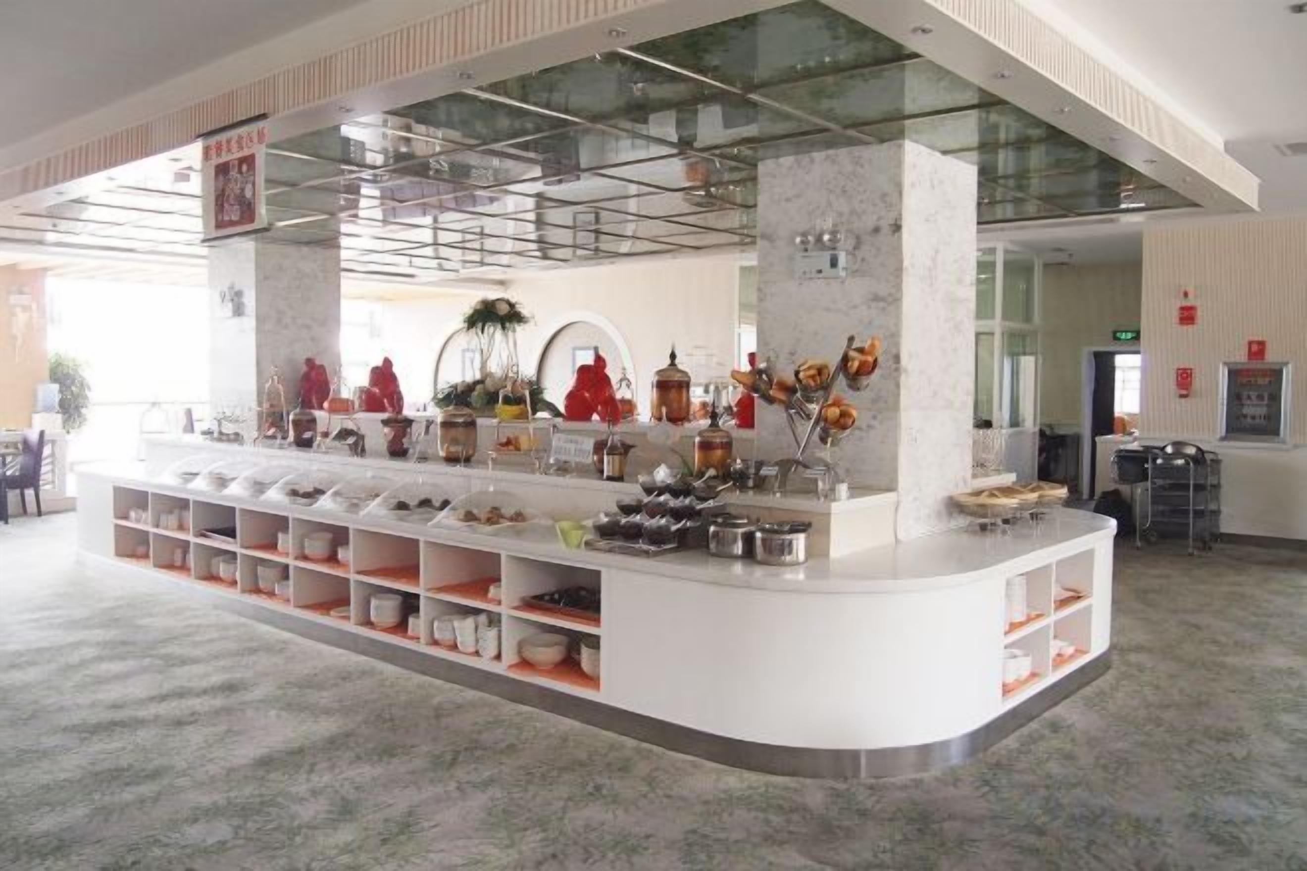 A modern hotel lobby with a central reception desk, a glass ceiling, and a variety of amenities including a buffet area.