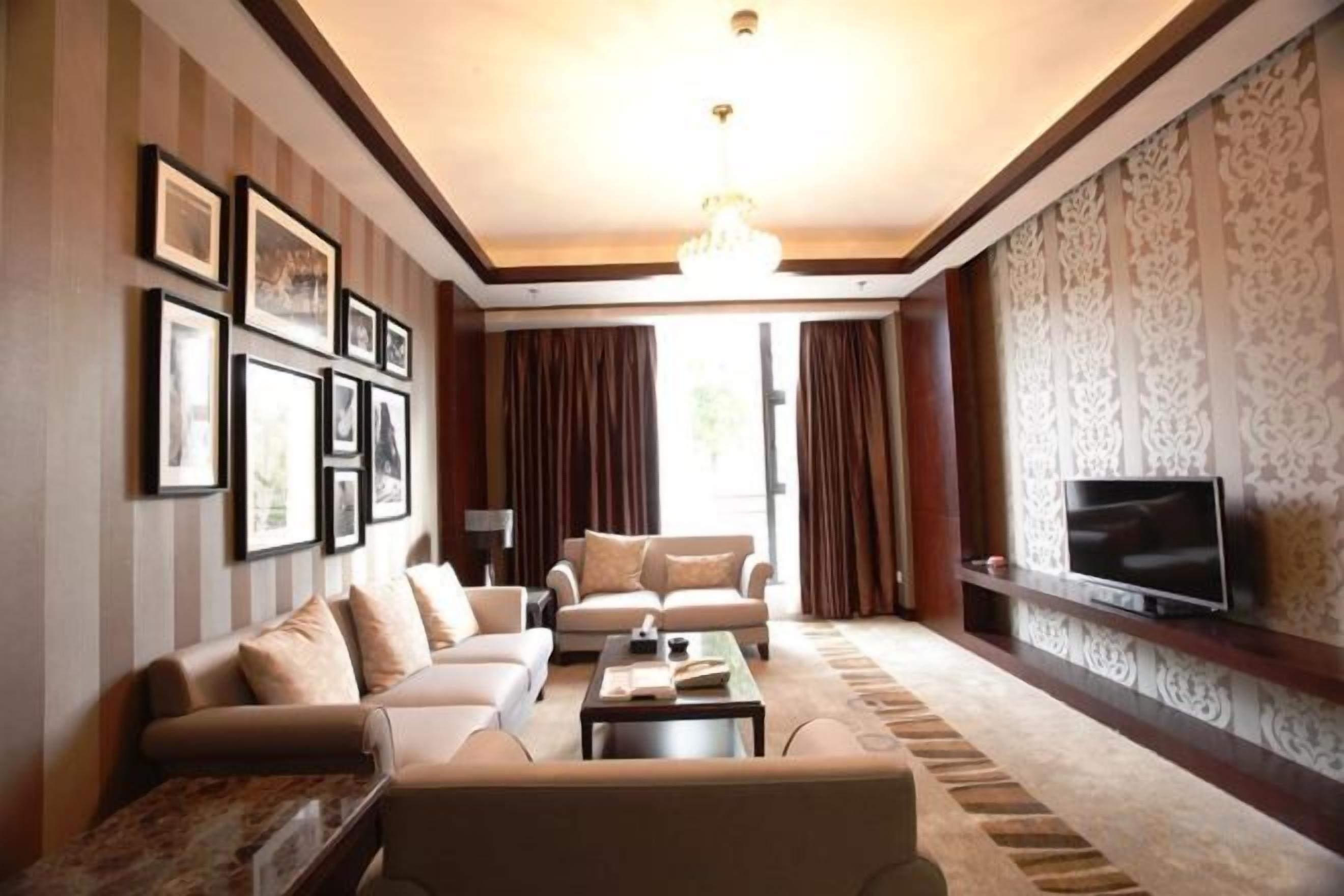 A living room with a sofa set, a coffee table, a flat-screen TV mounted on the wall, and a patterned wallpaper.