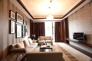 A living room with a sofa set, a coffee table, a flat-screen TV mounted on the wall, and a patterned wallpaper. - Chuntian Wenti Huiguan Hotel (Kunming)