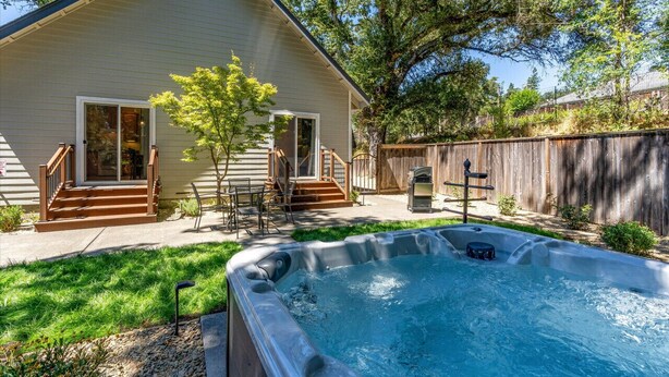 A house with a hot tub in the backyard, a wooden deck, and a covered patio area.