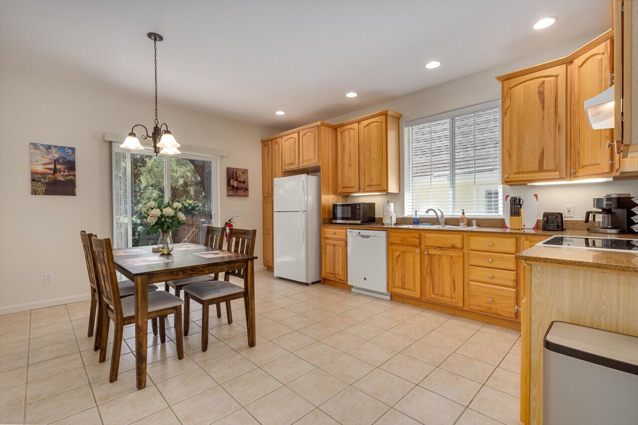 A modern kitchen with wooden cabinets, a dining table with chairs, a refrigerator, a microwave, and a dishwasher.