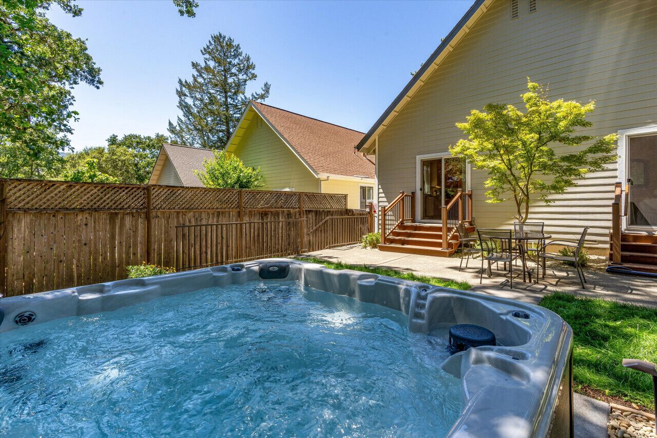 Un patio trasero con jacuzzi, cerco de madera y una casa con porche.