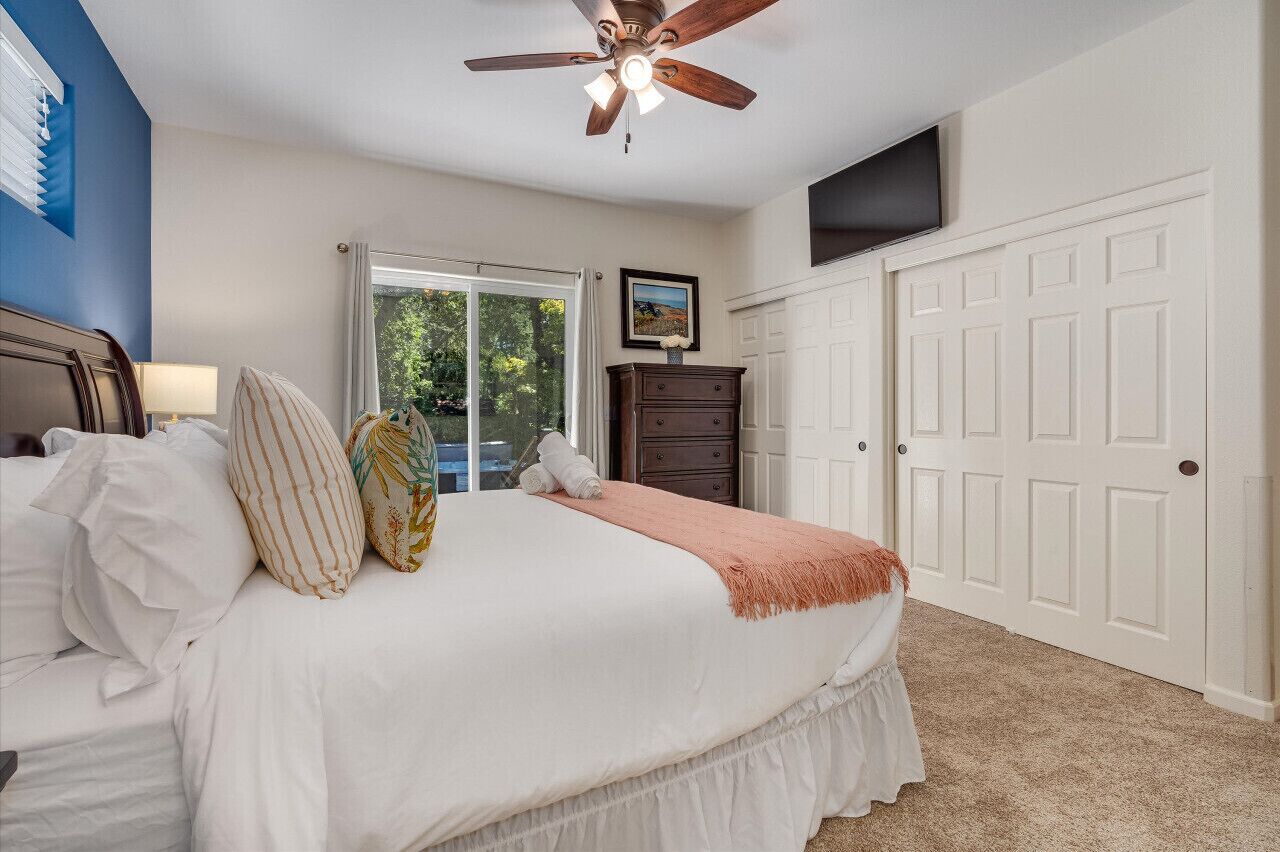 A bedroom with a bed, a ceiling fan, a dresser, a TV, and a door.
