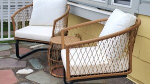 Deux fauteuils à bascule en osier, dotés de coussins blancs, sur une terrasse en pierre.