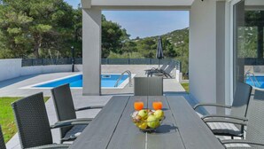 Een zwembadterras met een tafel gedekt voor twee personen, een schaal fruit en twee glazen sinaasappelsap.