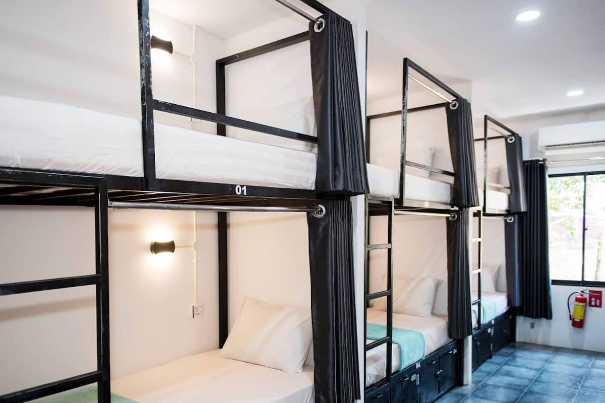 A dormitory room with bunk beds, a window with curtains, and a tiled floor.