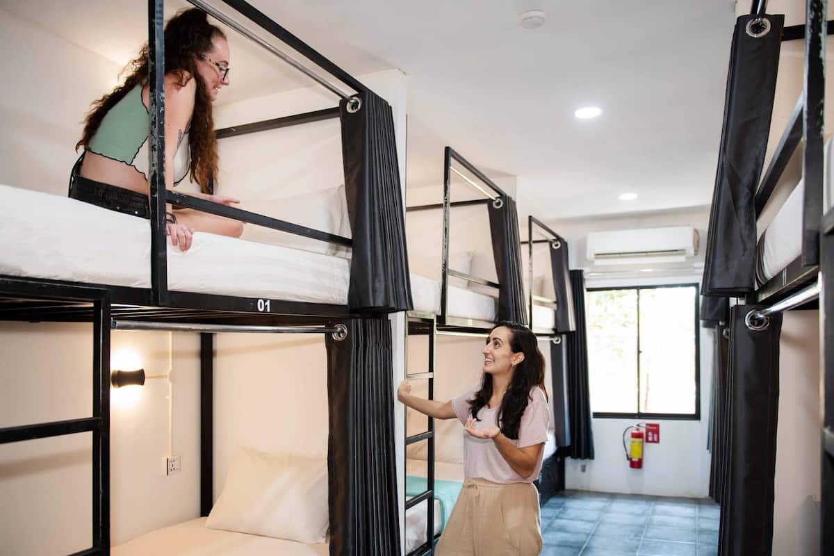 A dormitory-style room with bunk beds, numbered beds, and a fire extinguisher on the wall.