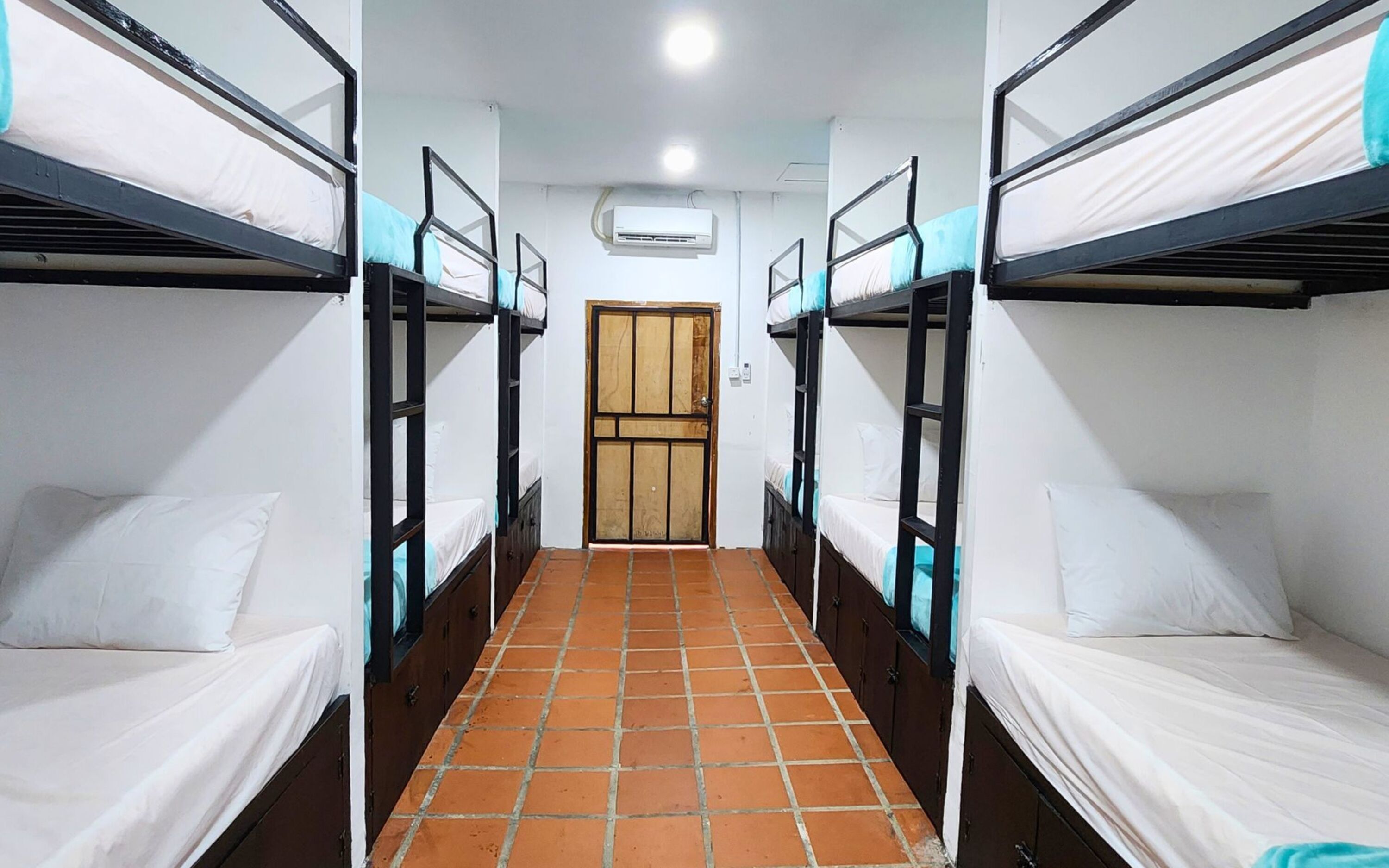 Un pasillo con literas a ambos lados, suelo de baldosas y una puerta al final.