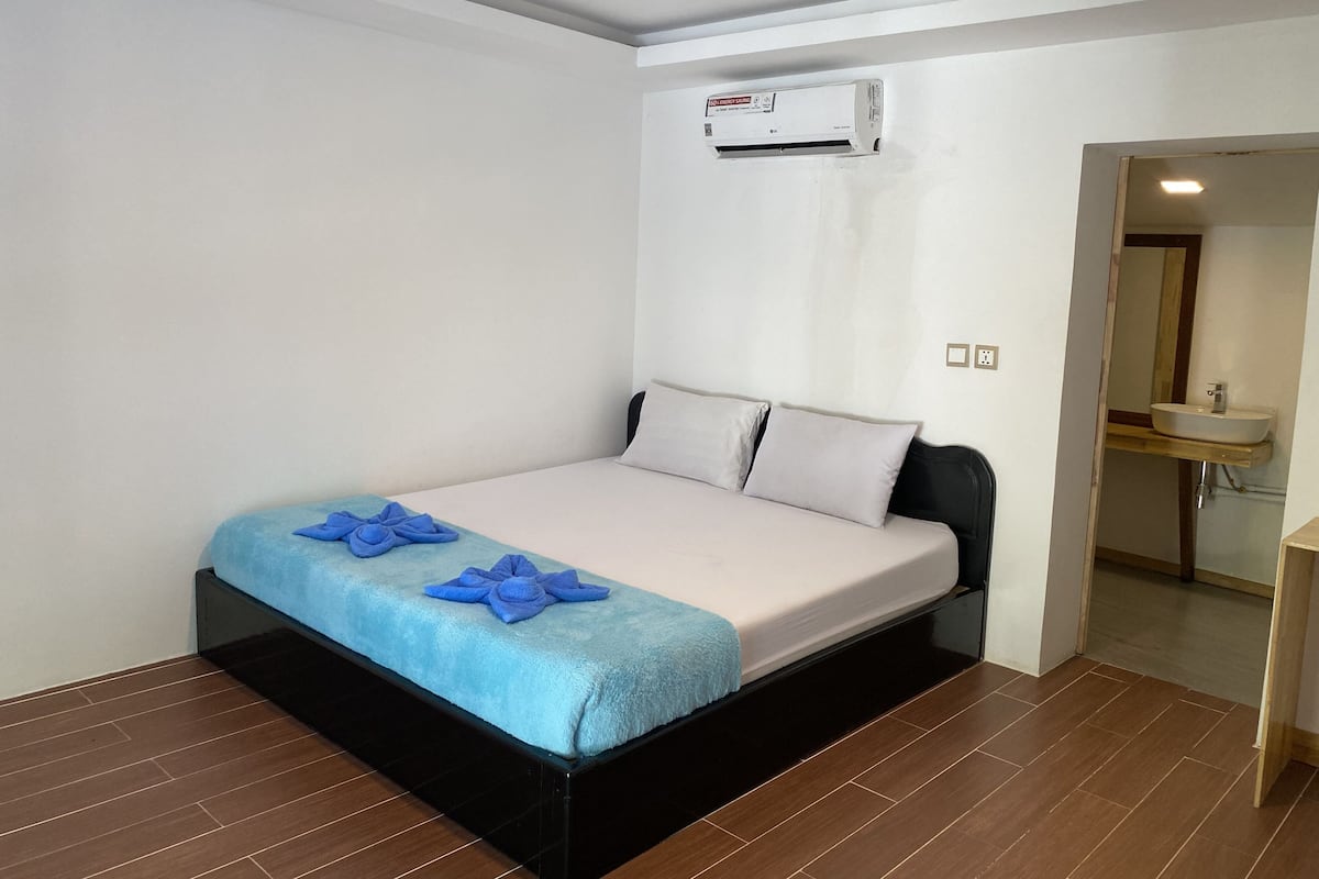 A hotel room with a bed, a bathroom with a sink, and an air conditioning unit on the wall.