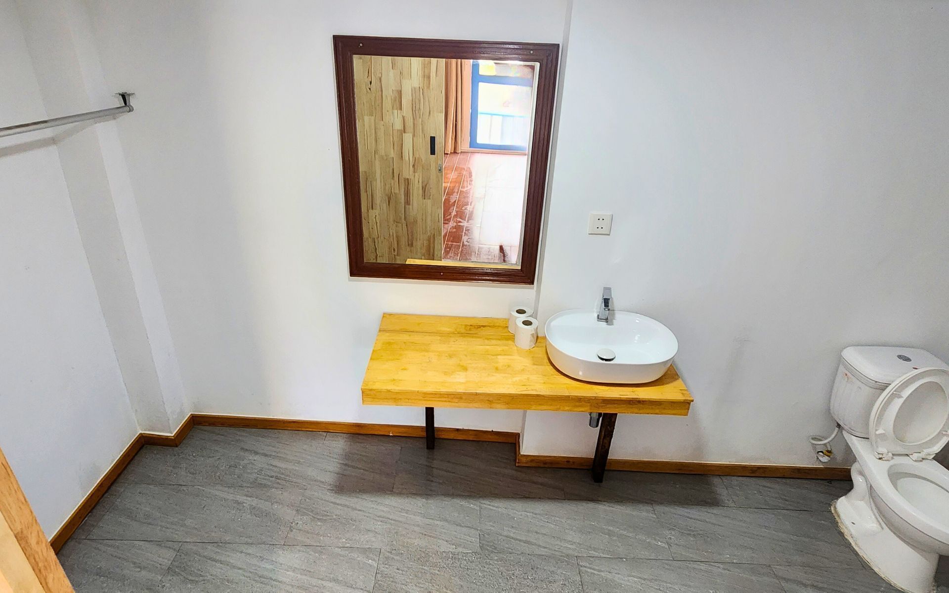 A small bathroom with a wooden vanity, a white sink, and a toilet.