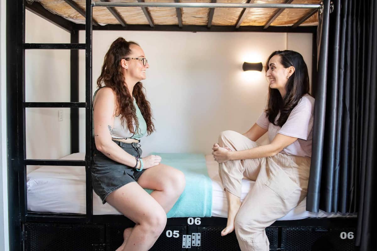A bunk bed room with two occupants, one sitting on the lower bunk and the other on the upper bunk.