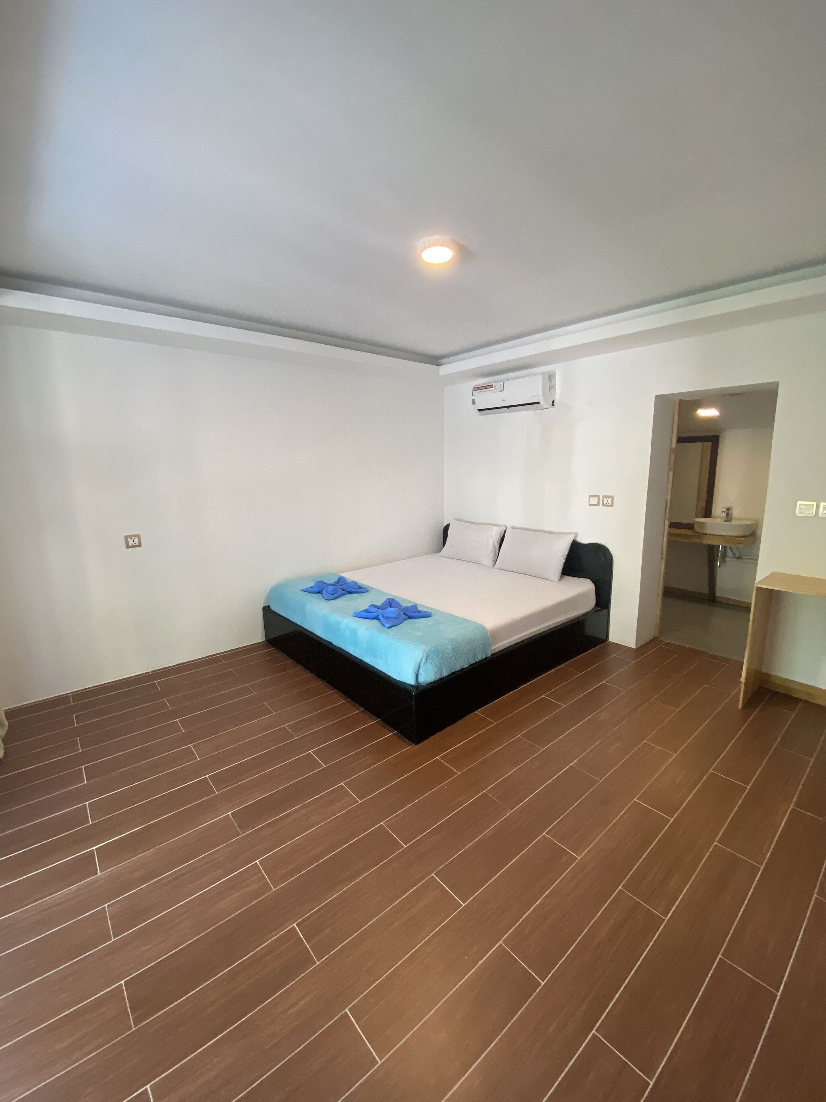 A bedroom with a bed, a wooden floor, a white wall, and an air conditioning unit.