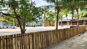 A beachside resort with bamboo fences, palm trees, and blue-roofed buildings.