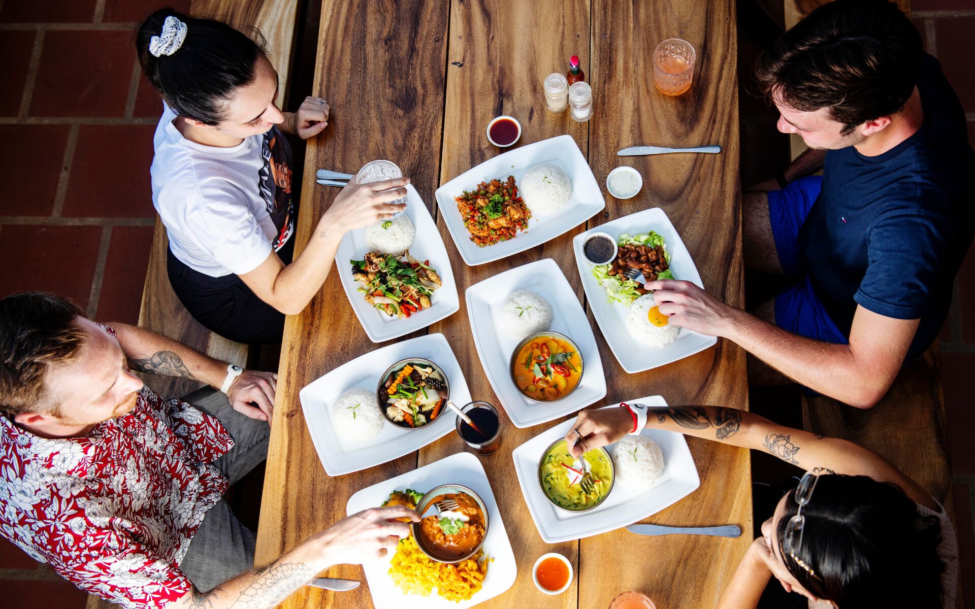 A group of people dining at a wooden table with various dishes, including rice, curry, and a bowl of soup.