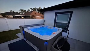 Un jacuzzi dans un jardin, avec une fenêtre et une clôture blanche.