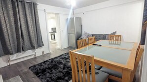 Ein kompakter Wohnraum mit Esstisch, Stühlen, einer Couch, einem Kühlschrank und einem flauschigen, schwarzen Teppich.