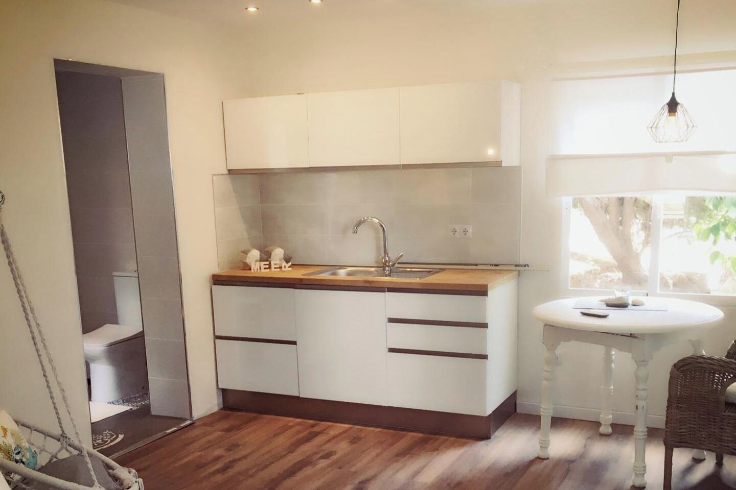 Une cuisine compacte avec des meubles blancs, un plan de travail en bois, un évier et une petite table à manger.