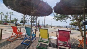 Buiten zitplaatsen met parasols, uitzicht op het strand en palmbomen.