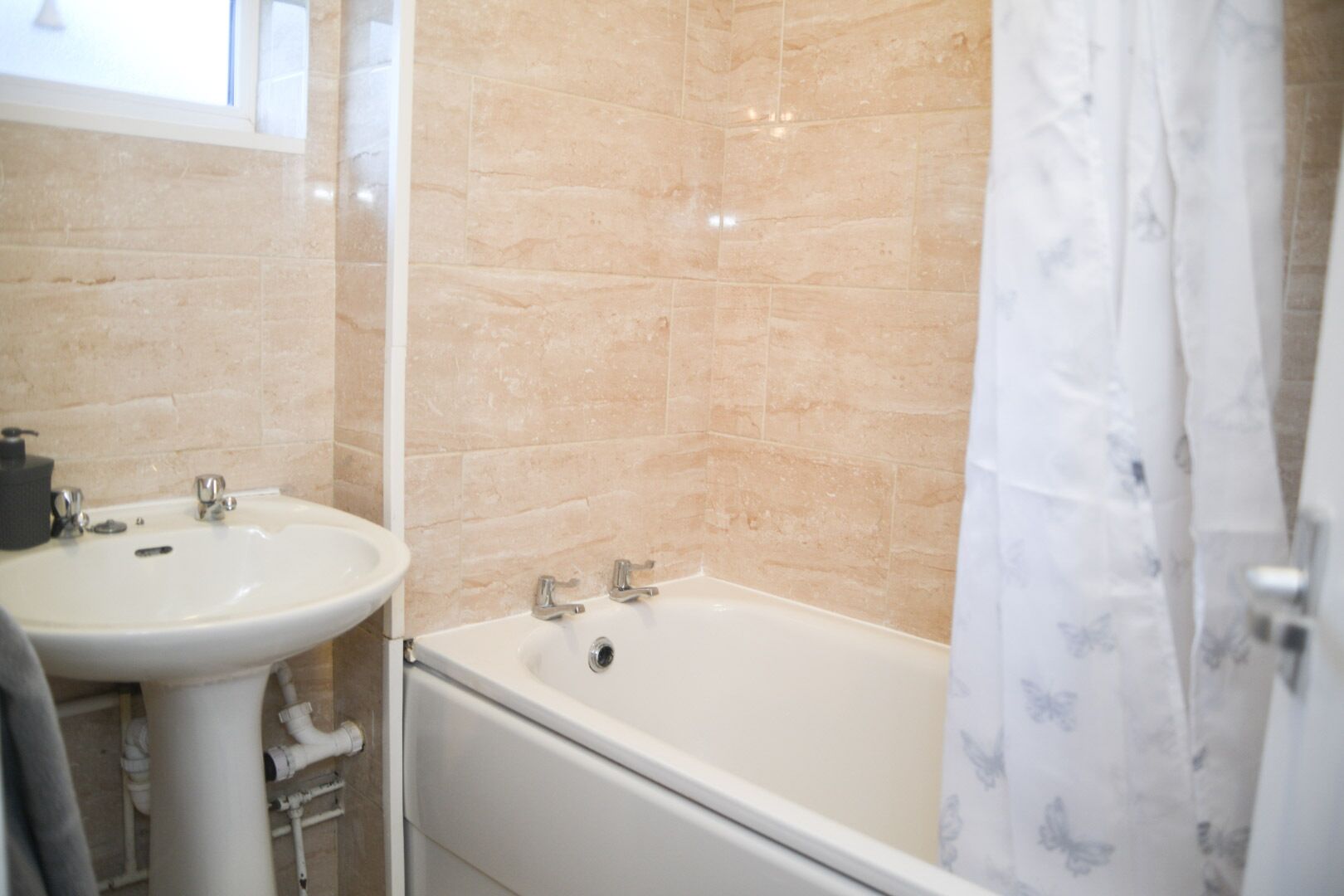 Une salle de bain avec un lavabo blanc, une baignoire et des murs recouverts de carreaux beiges.