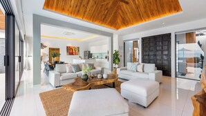 A modern living room with a wooden ceiling, white sofas, a coffee table, and a large window.