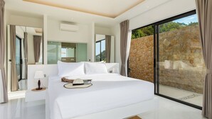 A modern hotel room with a large bed, a bedside table, a mirror, and a view of a stone wall through a glass door.