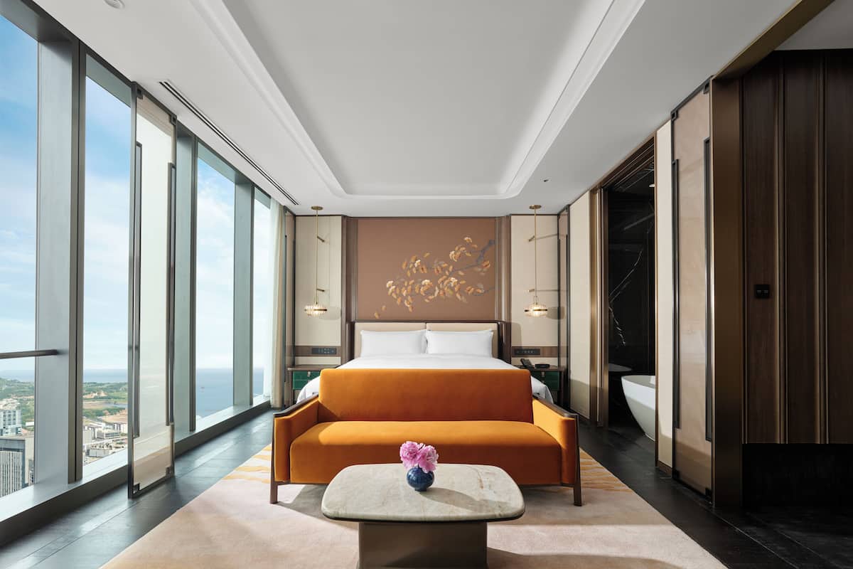 Una habitación de hotel moderna con una cama grande, un sofá, una mesita con un florero y vistas a la ciudad.