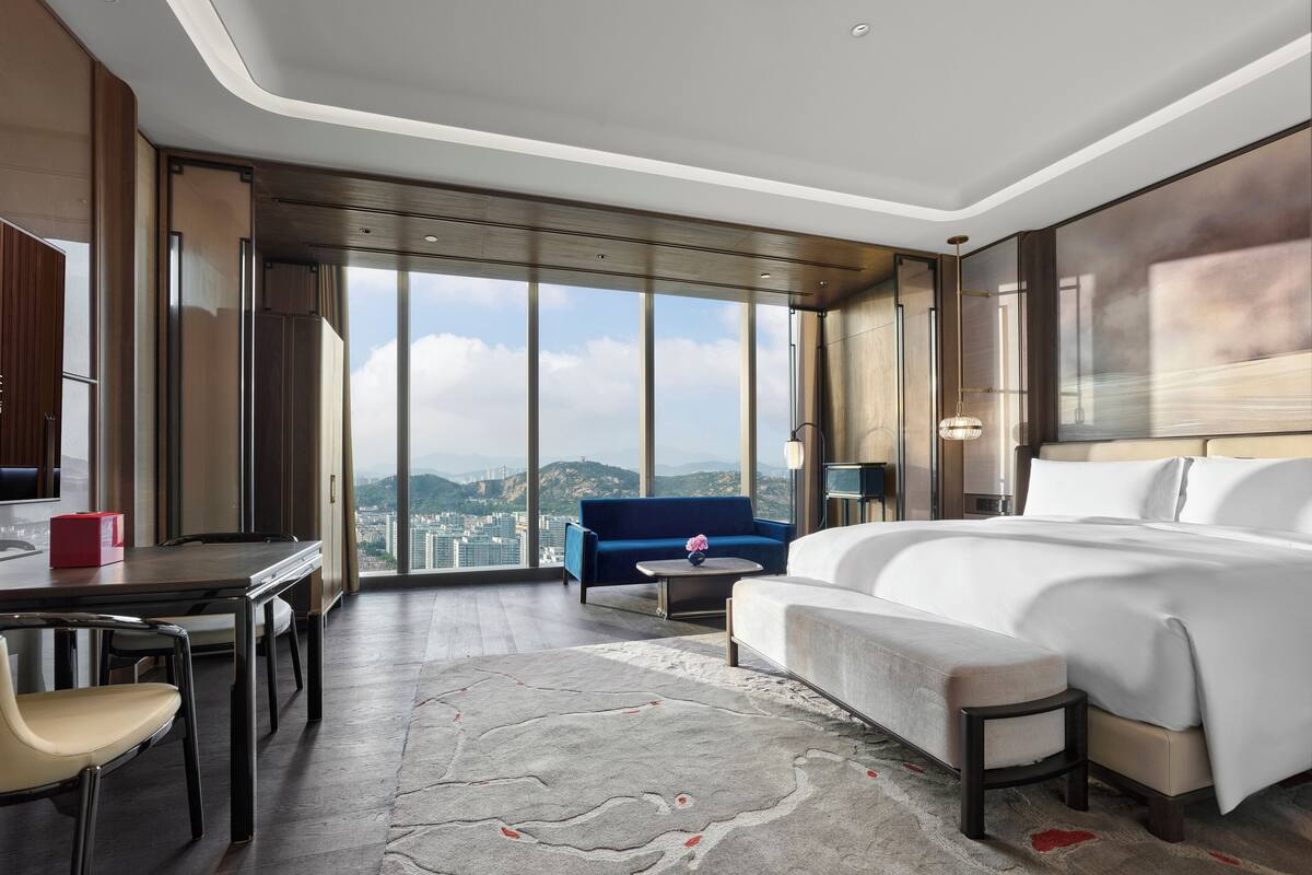 Una habitación de hotel moderna con una cama grande, un sofá, un escritorio y vistas a la ciudad.